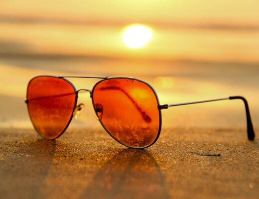 red lens sunglasses on sand near sea at sunset selective focus photography